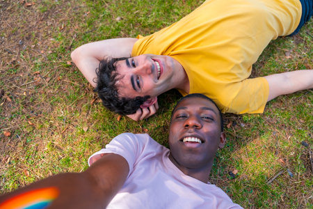 Portrait of a couple of multi-ethnic men in a park, lgbt concept, lying on the grass taking a selfieの写真素材