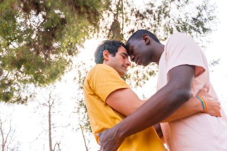 lgbt concept, couple of multiethnic men in a park in a romantic pose under a treeの写真素材