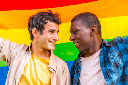 Portrait of multiethnic gay male couple holding a rainbow lgbt symbol flagの写真素材