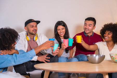 Group of friends eating popcorn and laughing while watching funny movie on TV at homeの写真素材