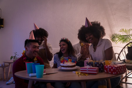 Multi-ethnic group of friends at a birthday party on the sofa at home with a cake and gifts, applauding after blowing out the candlesの写真素材