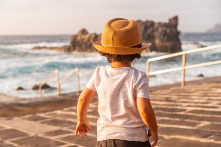 Boy from behind with hat smiling at summer sunset on the beach, summer vacationの写真素材