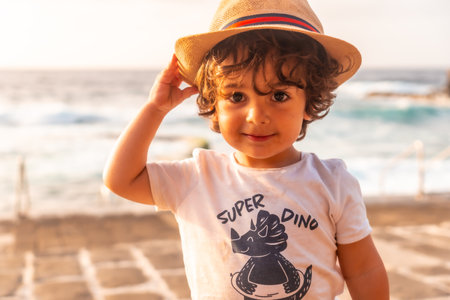 Portrait of cute little boy in hat smiling at summer sunset on the beach, summer vacationの写真素材