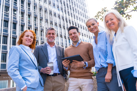 Portrait of cheerful group of coworkers laughing and looking at a tablet outdoors in a corporate office area, businesswoman and businessman and executives in commercial areaの写真素材