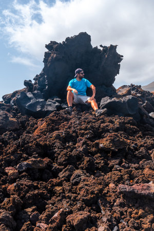 Young tourist sitting on the red stones on the volcanic trail in the village of Tamaduste on the coast of the island of El Hierro, Canary Islands, Spainの写真素材