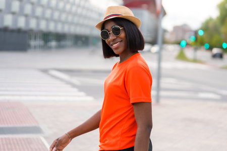 Young black woman tourist with orange t-shirt and sunglasses, posing for lifestyle photos in the city during summerの写真素材