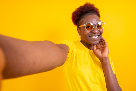 Young african american woman isolated on a yellow background smiling and making a selfie, studio shootの写真素材