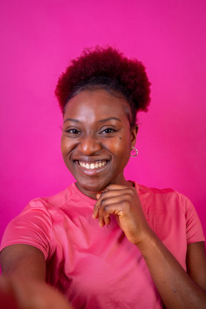 Young african american woman isolated on a pink background smiling with the victory gesture, studio...