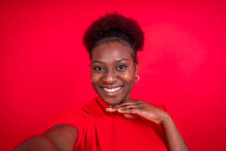 Young african american woman isolated on a red background smiling and making a selfie, studio shoot