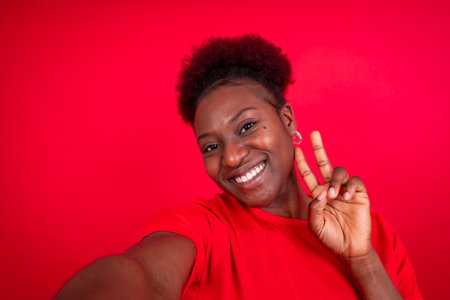Young african american woman isolated on a red background smiling and making a selfie, studio shootの写真素材