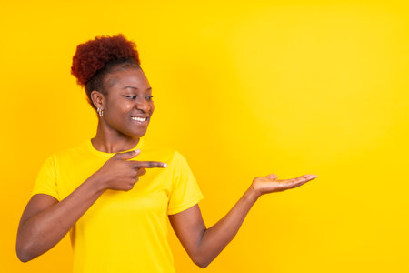 Young African American woman isolated over yellow background smiling and pointing, studio shoot, copy spaceの写真素材