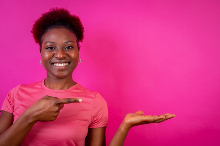 Young African American woman isolated over pink background smiling and pointing, studio shoot, copy spaceの写真素材