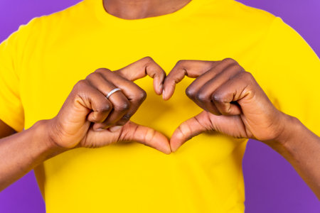 Young african american woman isolated on a purple background smiling and heart gesture, studio shootの写真素材
