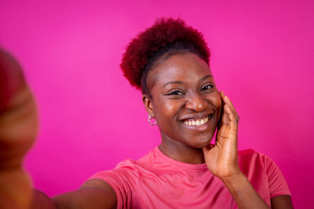Young african american woman isolated on a pink background smiling and making a selfie, studio shoot