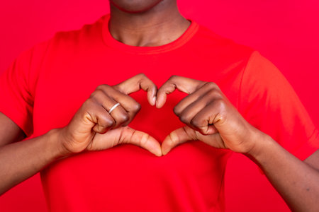 Young african american woman isolated on a red background smiling and heart gesture, studio shootの写真素材