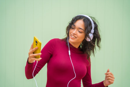 Portrait of latin woman with headphones smiling, technology concept on a green background, listening to musicの写真素材