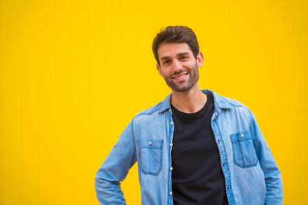 Portrait of an excited handsome man in basic clothes smiling isolated over yellow background