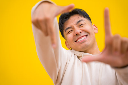 Portrait of south korean man in basic clothes over yellow background having fun and making take photo gestureの写真素材