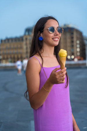 Portrait of young brunette woman eating a mango ice cream by the beach on summer vacation