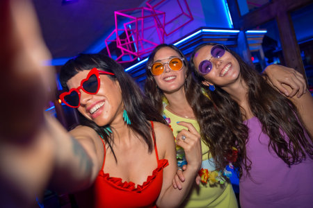 Female friends with sunglasses in a nightclub taking a selfie at a night party in a pubの写真素材