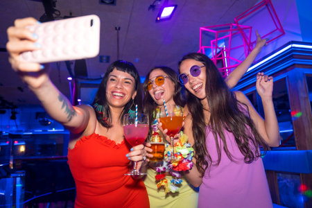 Friends with glasses of alcohol in a nightclub taking a selfie at a night party in a pubの写真素材