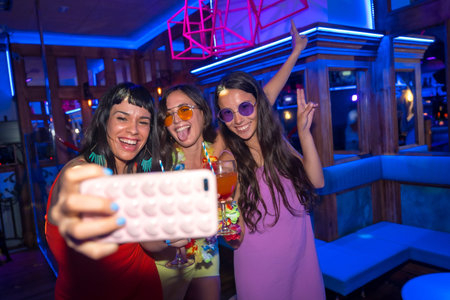 Smiling friends with glasses of alcohol in a nightclub taking a selfie at a night party