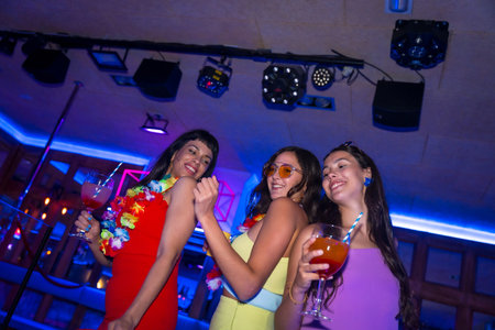 Female friends in a nightclub drinking glasses of alcohol smiling at a night partyの写真素材