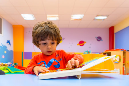 Portrait of a boy sitting at a table reading a story book, indoor of a kindergarten