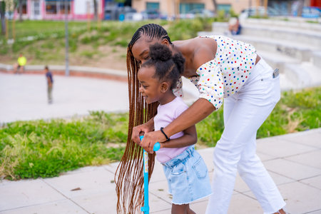 Black African ethnicity mother having fun with her daughter in playground, learning to ride a...
