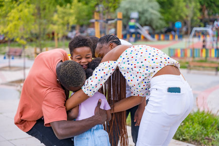 African black ethnic family with children in playground, hugging after schoolの写真素材