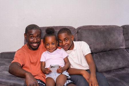 African black ethnic family father with children on sofa at home looking at phone