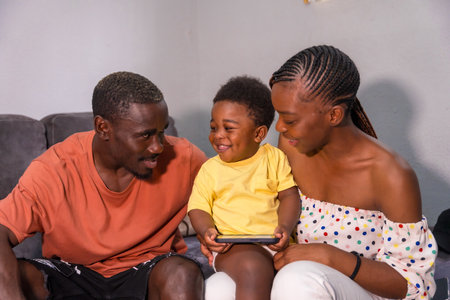 African black ethnicity family with their son on the sofa at home smiling and having fun with the phoneの写真素材