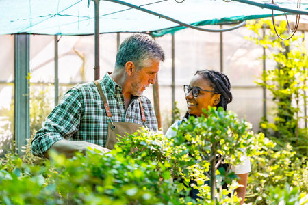Master gardener teaching flower nursery student girl checking plants in greenhouse