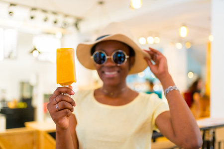 Black African ethnicity female customer eating a mango ice cream in a shopの写真素材