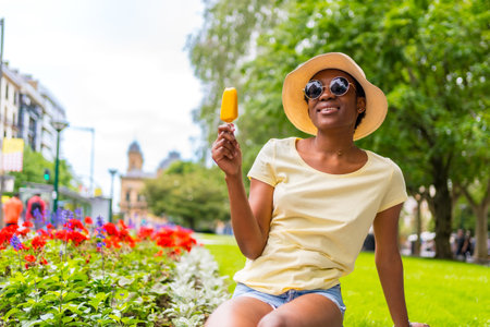 African black ethnicity woman eating a mango ice cream in the city, tourist enjoying summerの写真素材