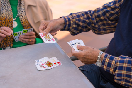 Hands of two elderly people in the garden of a nursing home or retirement home playing cards on a...