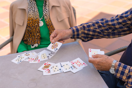 Hands of two elderly people in the garden of a nursing home or retirement home playing cards on a summer morningの写真素材