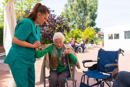 An elderly woman with the nurse in the wheelchair in the garden of a nursing home or retirement...