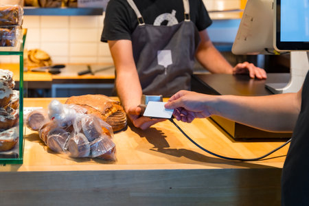 Customer in the bakery shop buying an artisan bread from the baker in the workshop, paying with the cardの写真素材