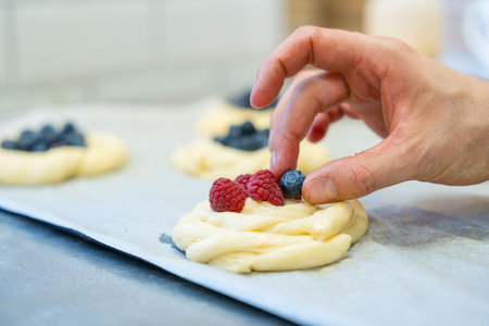 Baker of bakery in the workshop workshop of artisan bakery preparing the buns before baking and putting strawberriesの写真素材