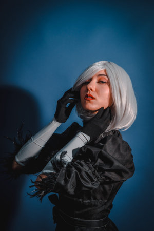 Portrait of cosplay woman in a black costume and a white wig in studio on a blue background