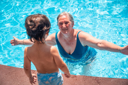 Mother and grandmother having fun with grandson in swimming pool on summer vacation, enjoying the...