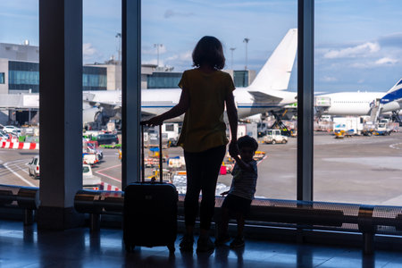 Silhouette of mother and son with luggage standing near the window in the airport, vacation conceptの写真素材