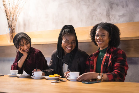 Portrait of three cheerful multicultural friends drinking coffee in a cafeteriaの写真素材