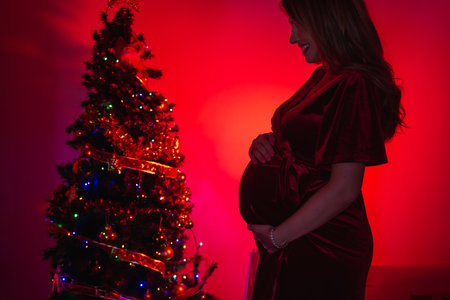 Silhouette of a beautiful pregnant woman decorating with the Christmas tree, with red lightの写真素材