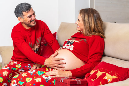 Young couple with decoration and red Christmas clothes touching the baby's bumps on the tummy....