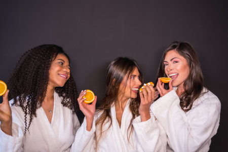 Studio photo with gray background of multi-ethnic relaxed women in bathrobe eating fruitの写真素材