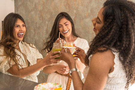 Three latin happy women celebrating with juices in a cafeteriaの写真素材