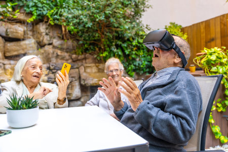 Elder man using virtual reality goggles sitting on the garden of a nursing homeの写真素材