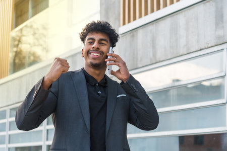 Horizontal portrait of a happy arab young businessman gesturing success while using phoneの写真素材